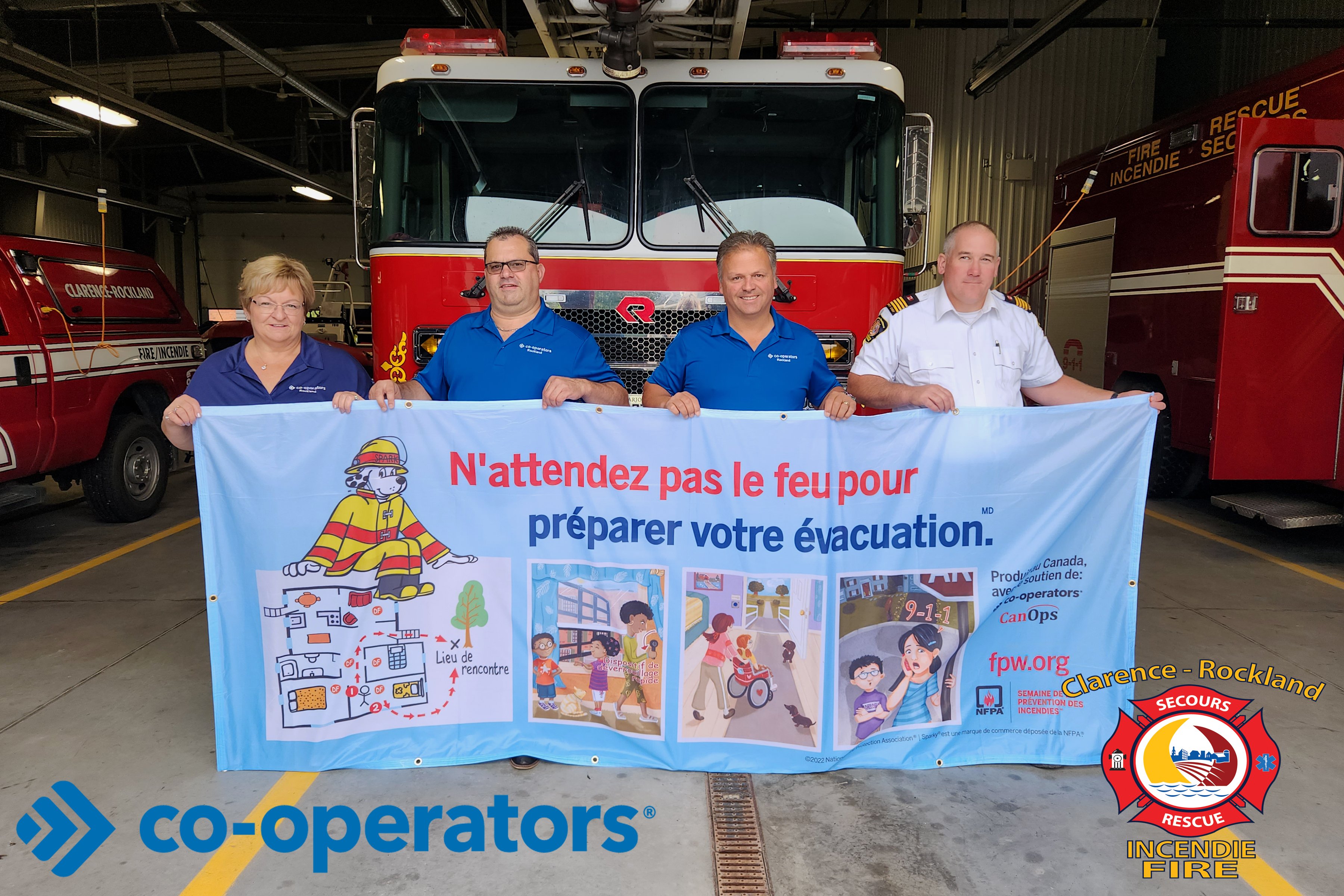 Rachelle Lodge, François Faucon, Daniel Lebrun et Martin Saumure tiennent un drapeau de la Semaine de prévention des incendies devant un camion de pompier