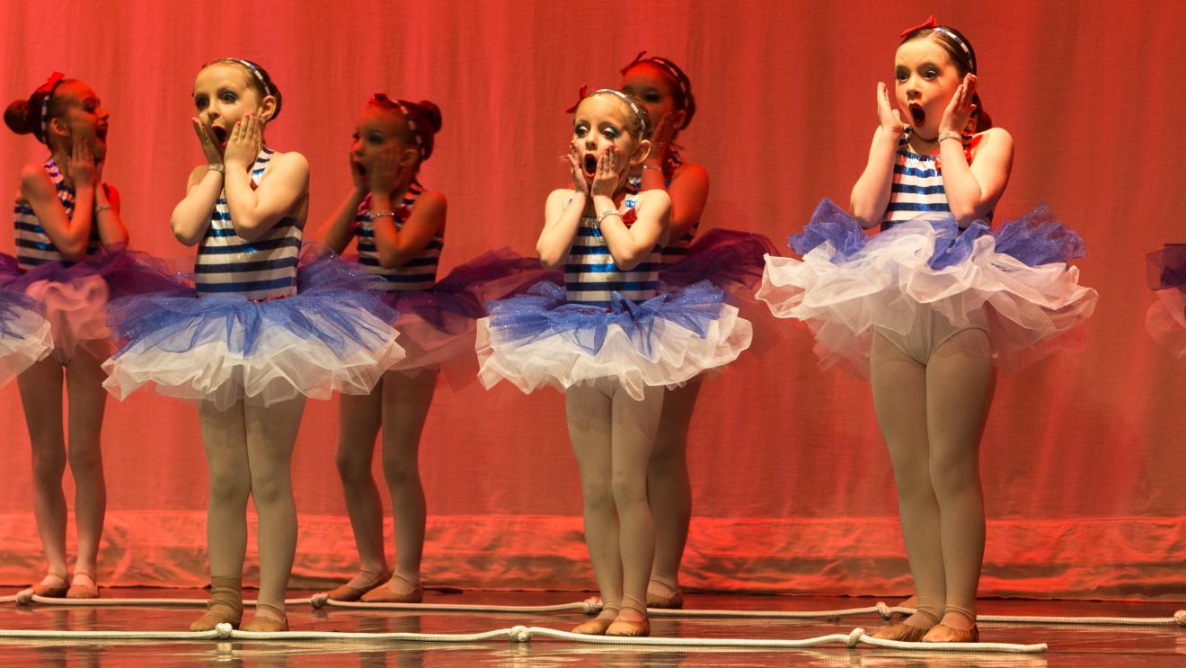 Danseuses en tutu bleu et blanc sur scène, éclairées en rouge.