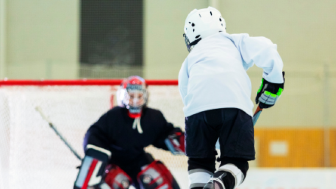 Hockey player in white jersey approaches goalie in black near the net.