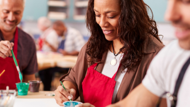 People painting at a workshop, wearing red aprons and smiling.