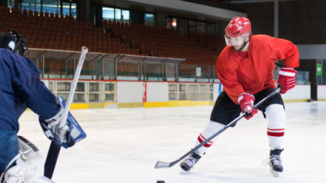 Ice hockey player in red jersey approaches goalie, preparing to shoot.