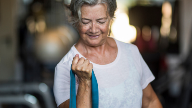 Elderly woman exercising with a resistance band in a gym.