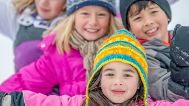 Kids in colorful winter clothes smiling in the snow.