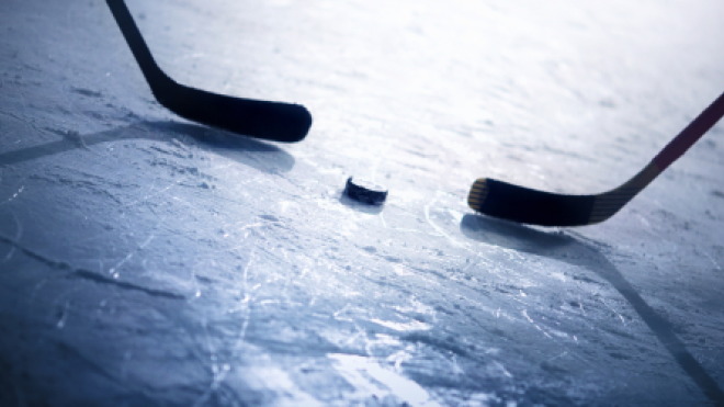 Hockey sticks face off with a puck on ice.