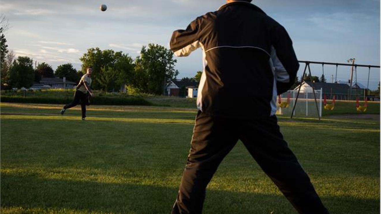 People playing catch on a grassy field at sunset.