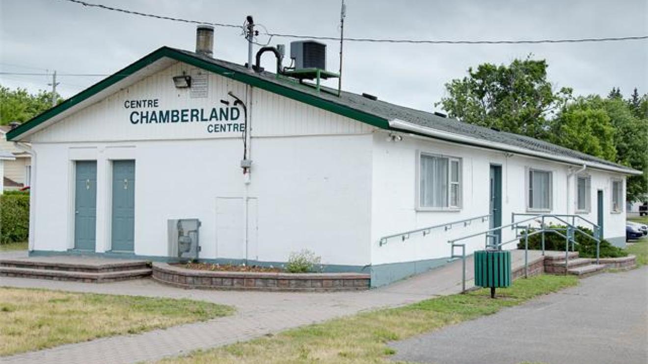 Single-story white building with a ramp and greenery. Cloudy sky above.