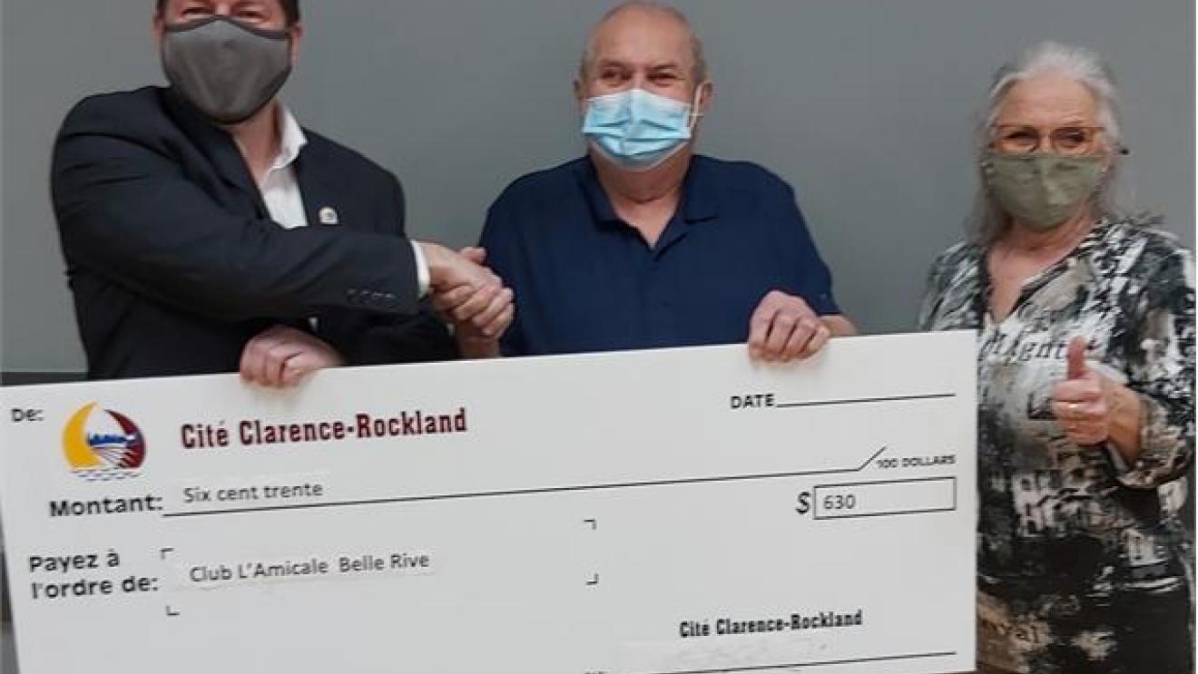 Three people holding a large check, all wearing face masks.