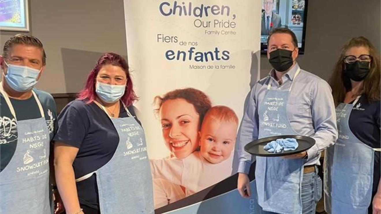 Four masked people in aprons stand by a banner with smiling adults and a child.