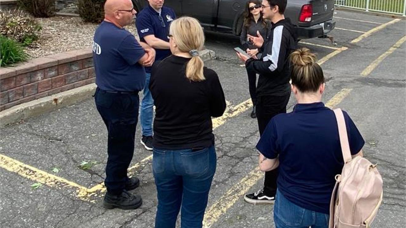 Group of people talking in a parking lot with parked truck nearby.