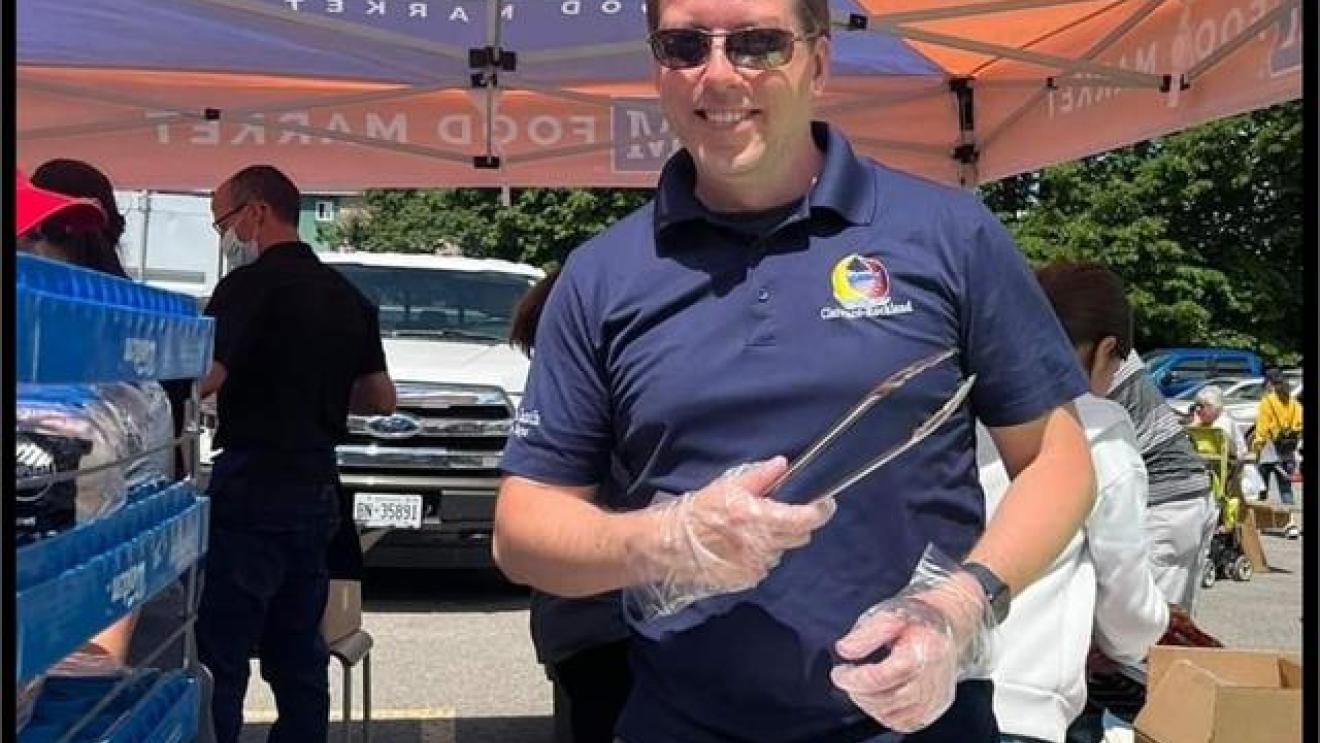 Man serving food at an outdoor event under an orange canopy.