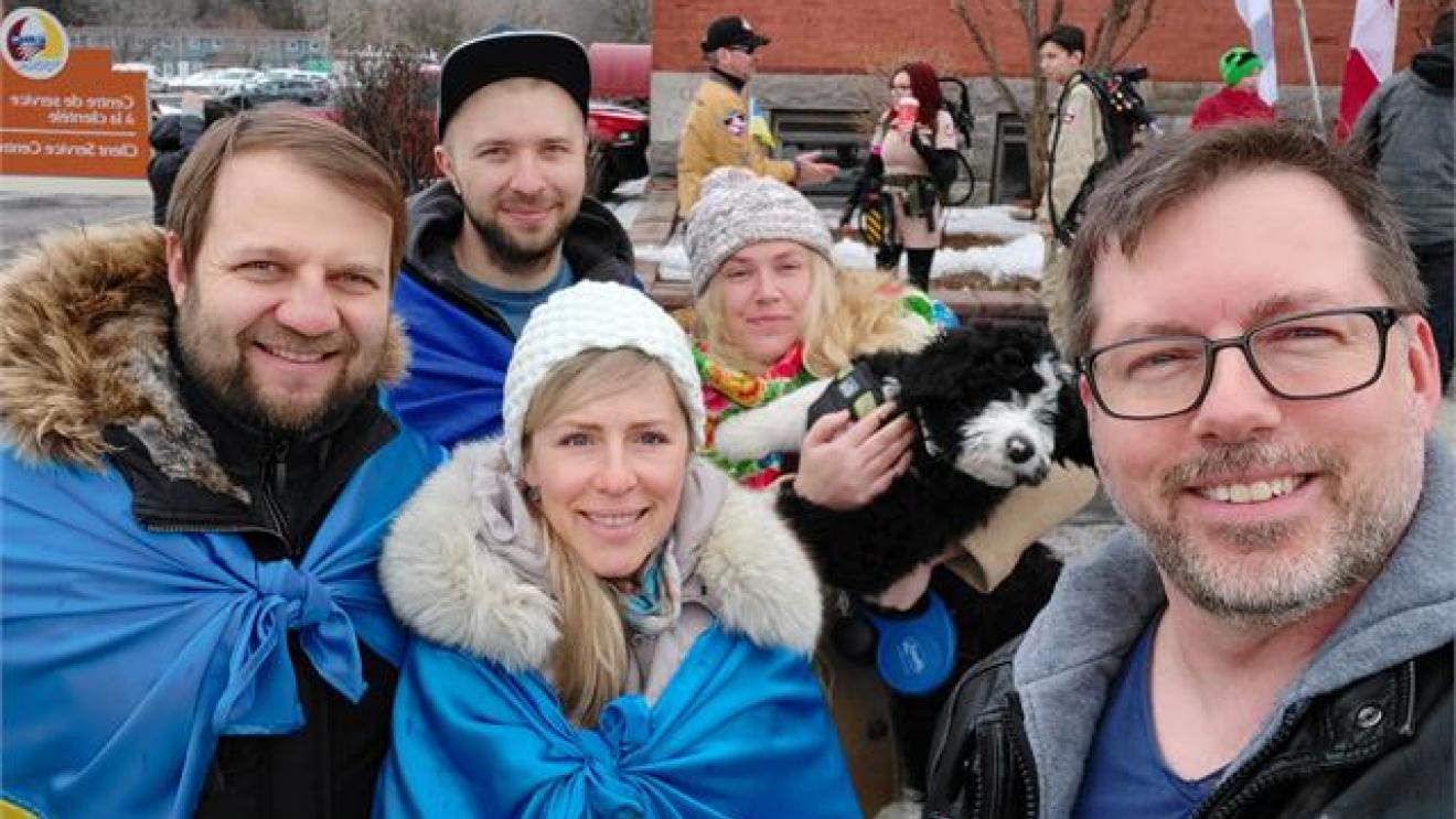 Group of people outdoors wearing blue, smiling, some with winter clothing.