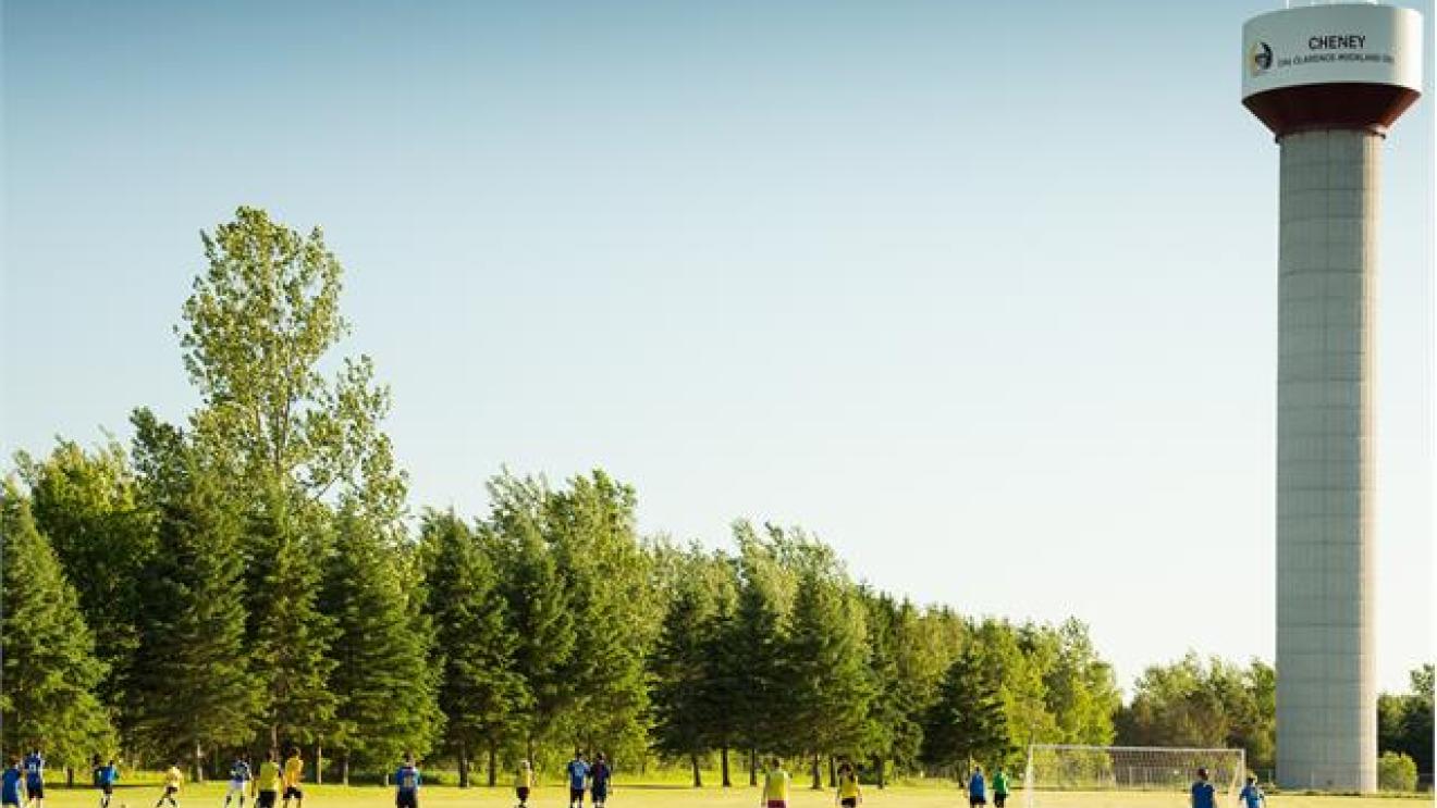 Soccer game on a grassy field, tall water tower and trees in the background.