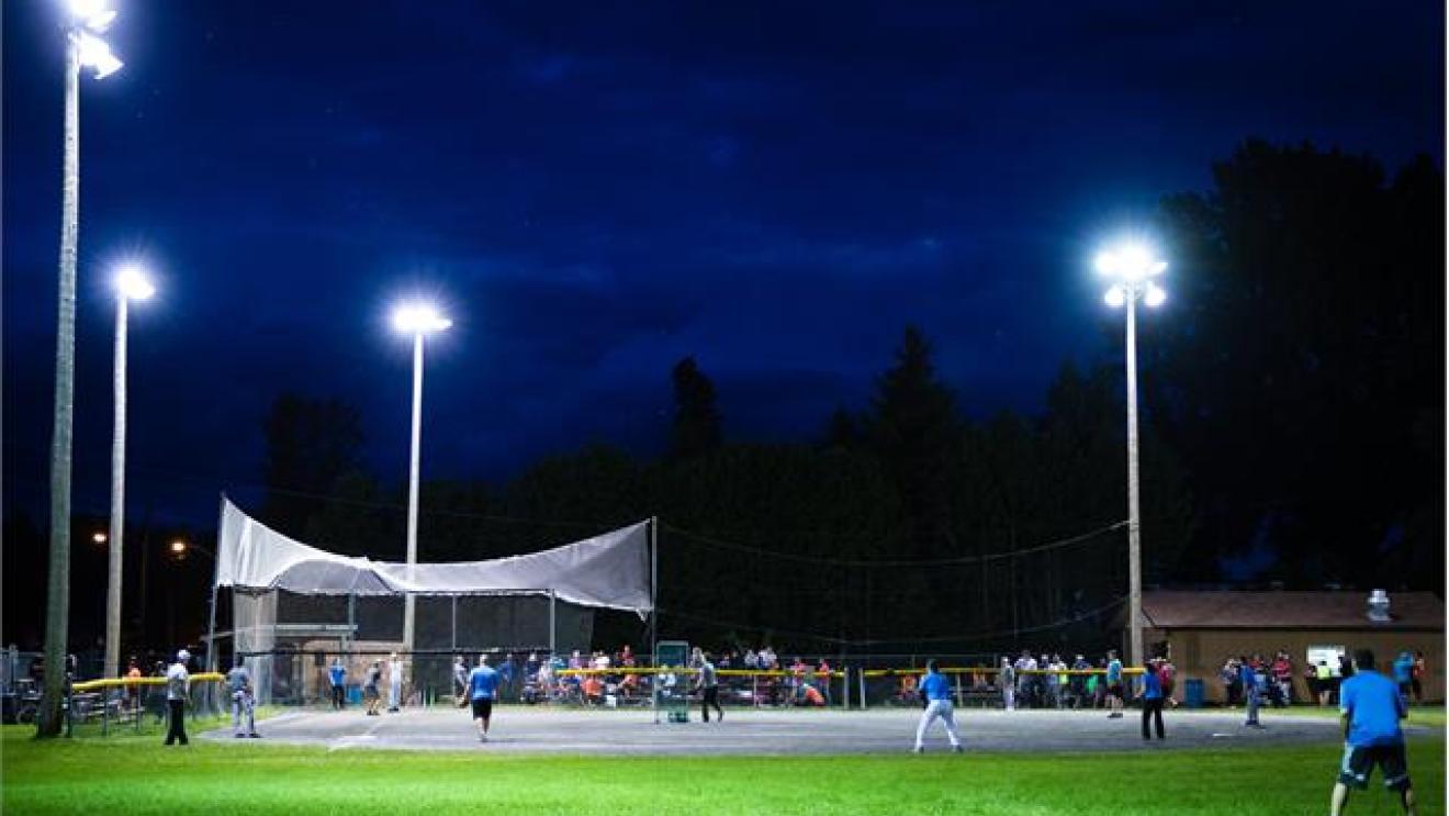 Nighttime baseball game under bright lights on a grassy field.