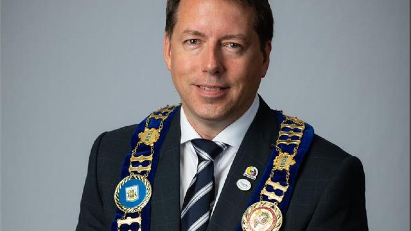 Man in a suit with a striped tie and chain of office, smiling.