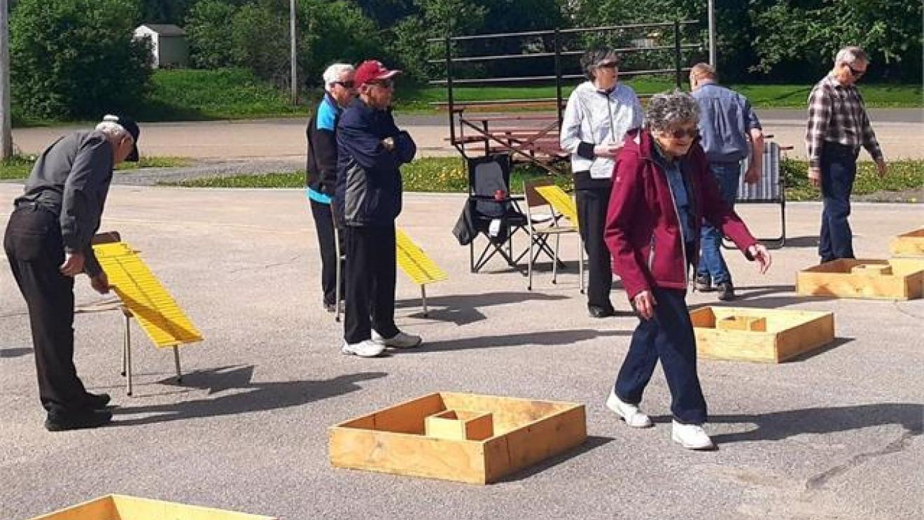 People playing outdoor games with wooden ramps and boxes in a sunny park.