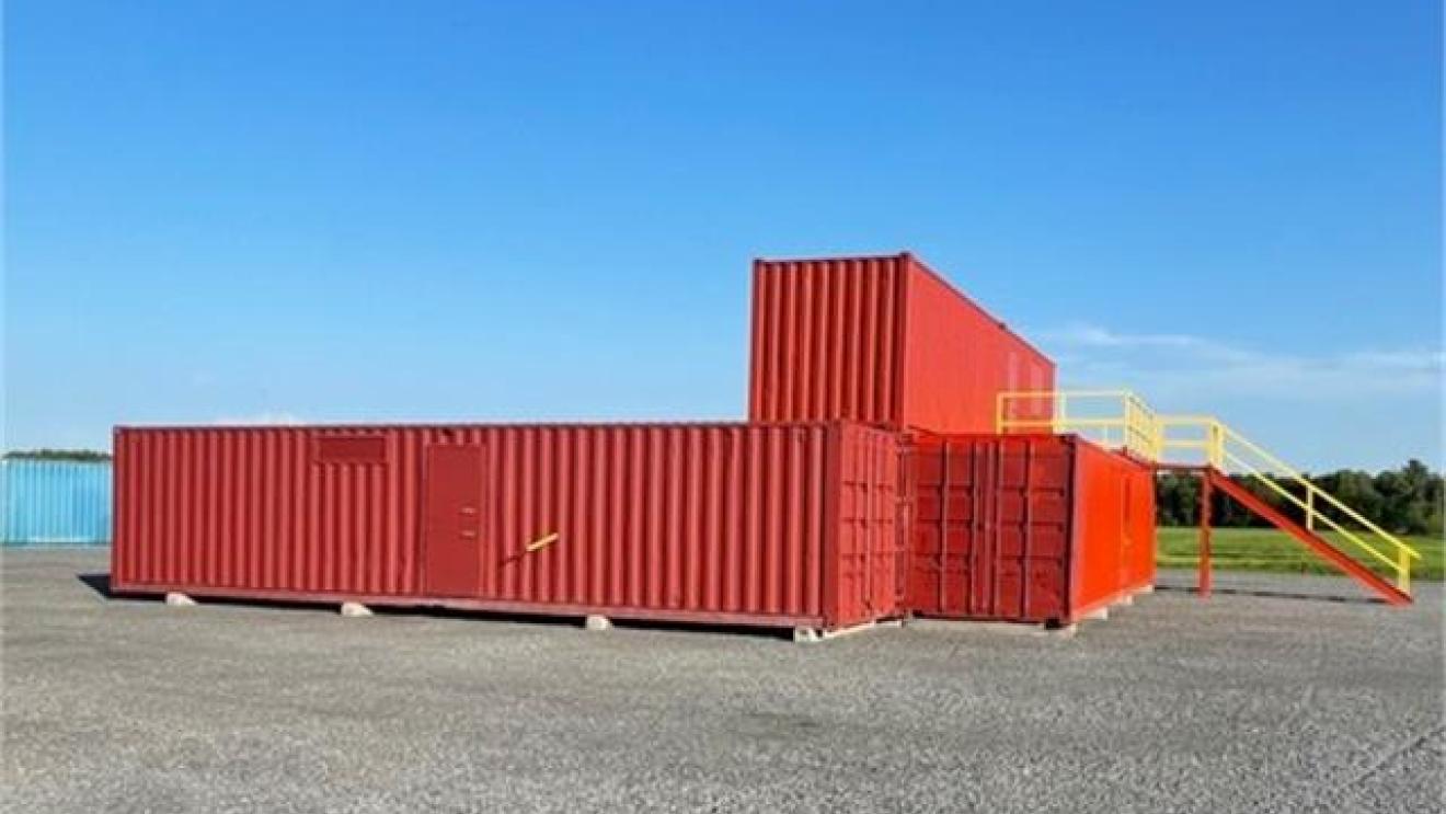 Red shipping containers stacked, yellow stairs, clear blue sky.