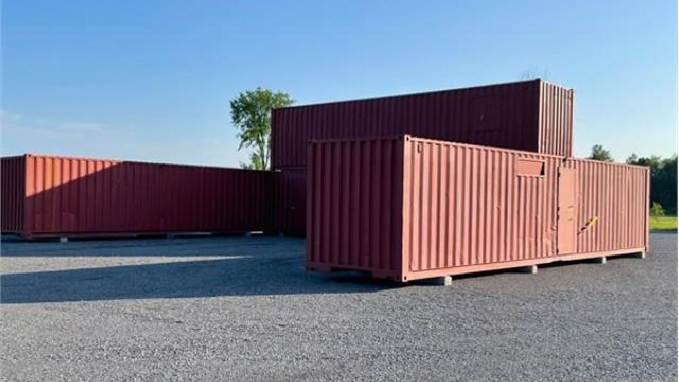 Red shipping containers stacked on gravel under a clear blue sky.