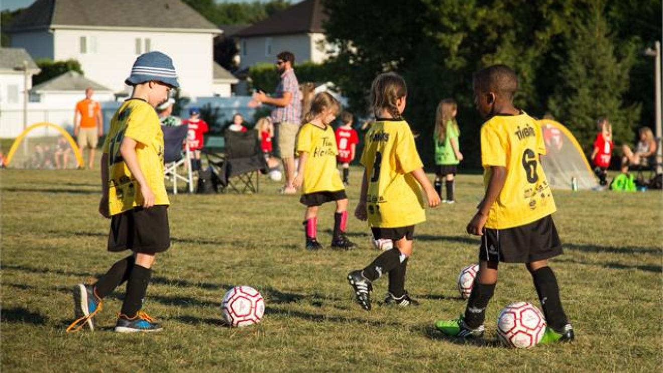 Kids in yellow jerseys playing soccer on a grassy field.