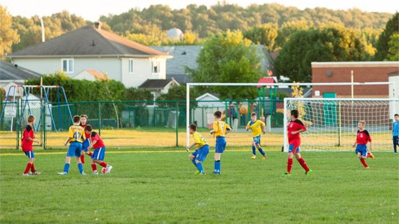 Kids playing soccer on a grassy field at sunset.