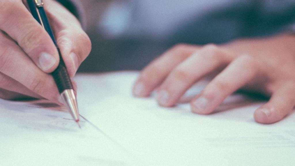 Hand writing with a pen on paper, office setting.