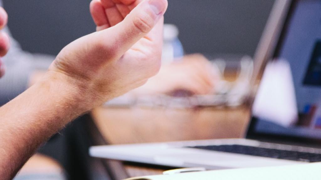 Man gesturing near a laptop with colorful screen in a meeting.