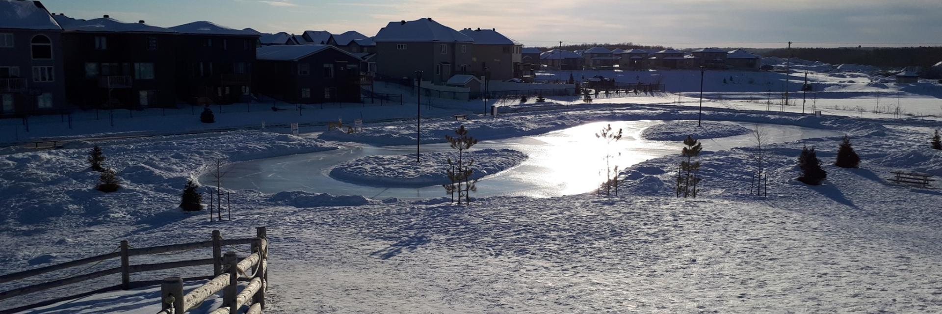 Snowy landscape with a fence and a pond under bright sunlight.