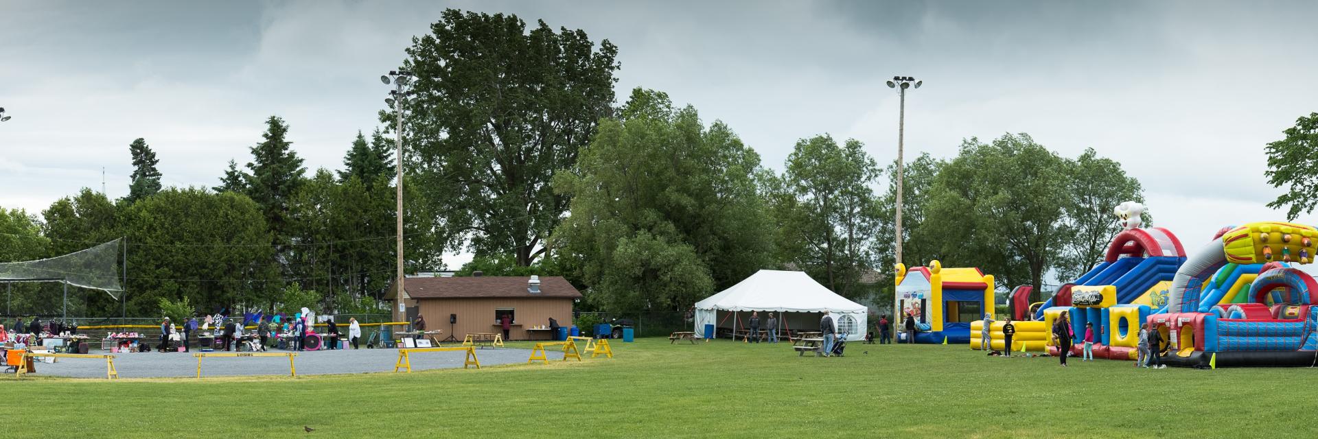 Outdoor event with bounce houses, tents, trees, and a cloudy sky.