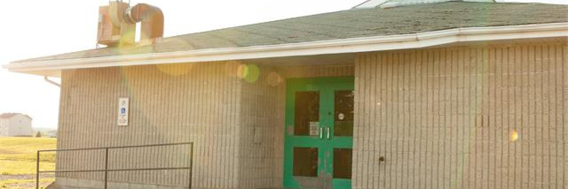 Small building with teal doors and a ramp, sunlit exterior.