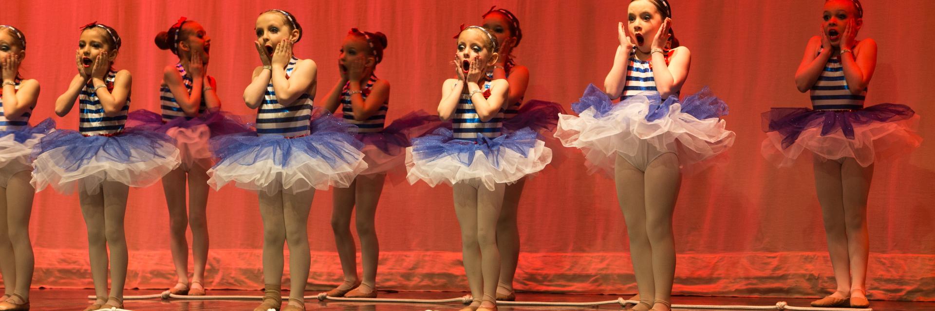Danseuses en tutu bleu et blanc sur scène, éclairées en rouge.