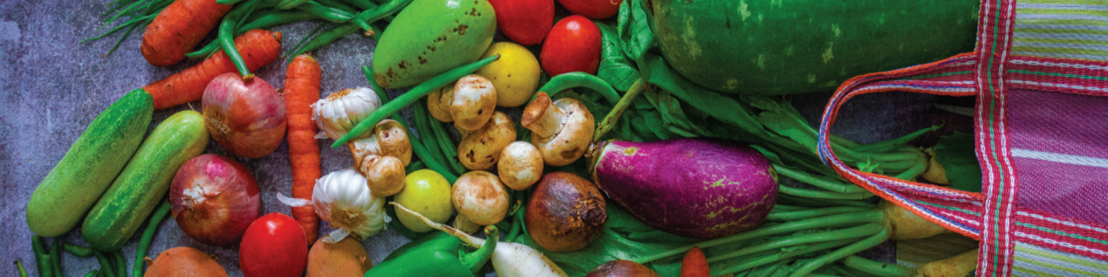 Assorted colorful vegetables with a striped tote bag.