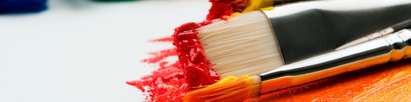 Paintbrushes with red and orange paint on canvas.