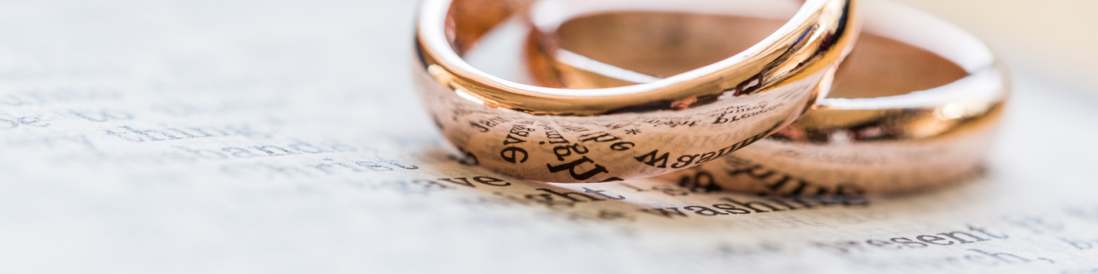 Two gold wedding rings on a blurred handwritten letter.