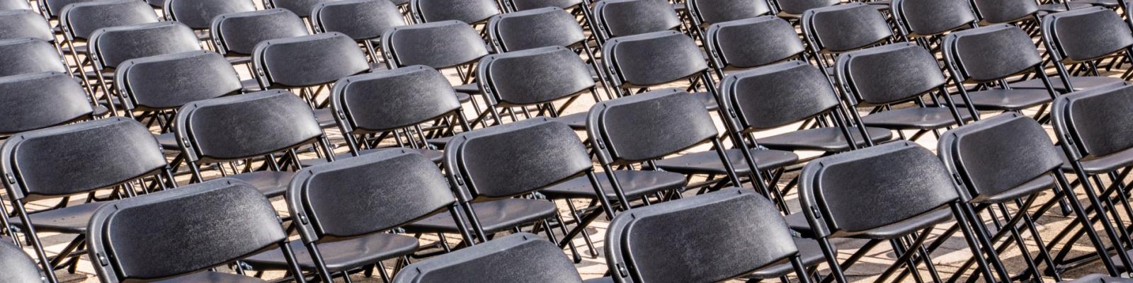 Rows of empty black folding chairs in sunlight.