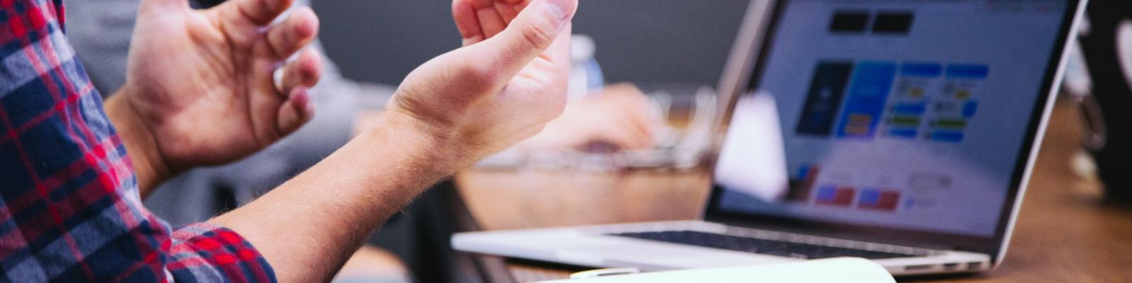 Man gesturing near a laptop with colorful screen in a meeting.