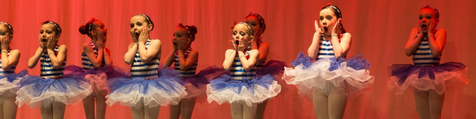 Young dancers in blue and white tutus perform on stage.