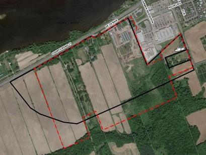 Vue aérienne par satellite montrant des terres agricoles, des zones boisées et des terrains aménagés avec des lignes de délimitation noires et rouges entourant un corridor proposé